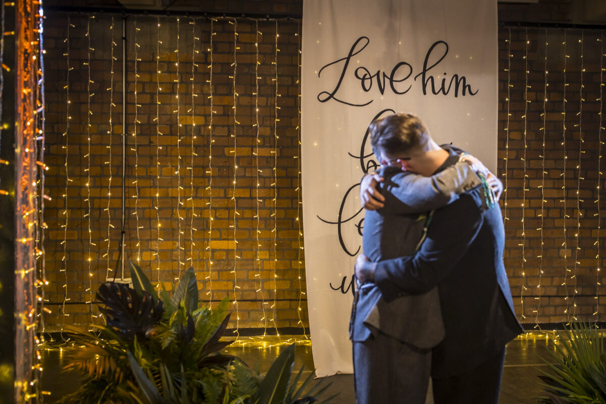 Two people hugging at an event with lights.
