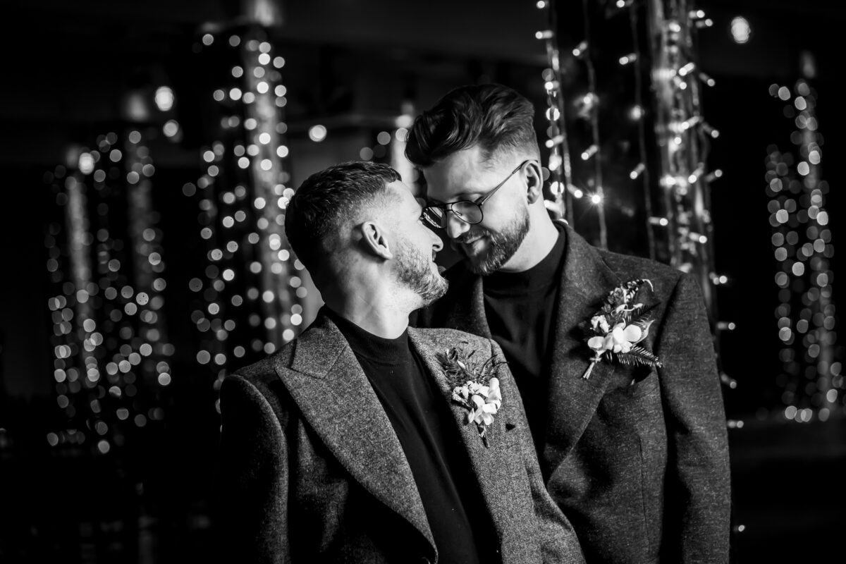 Same-sex couple hugging in festive lights.