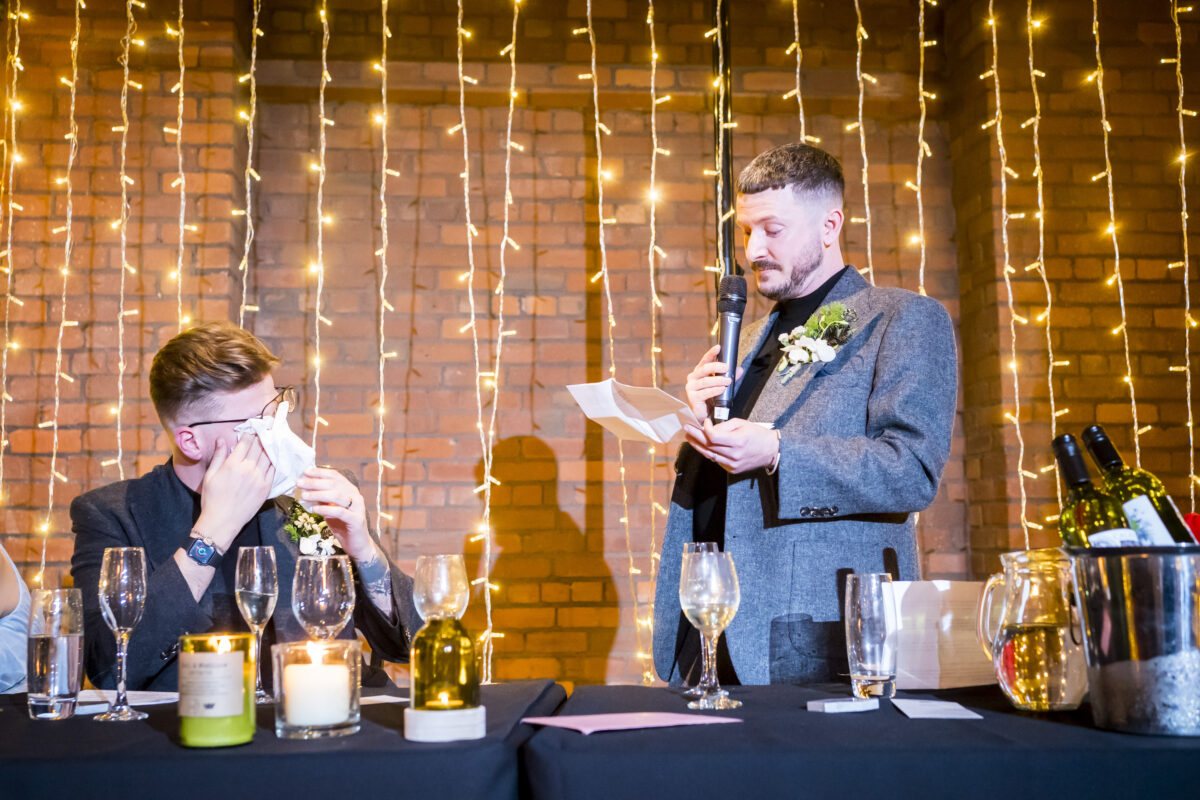 Groomsman giving emotional wedding speech with lights background.