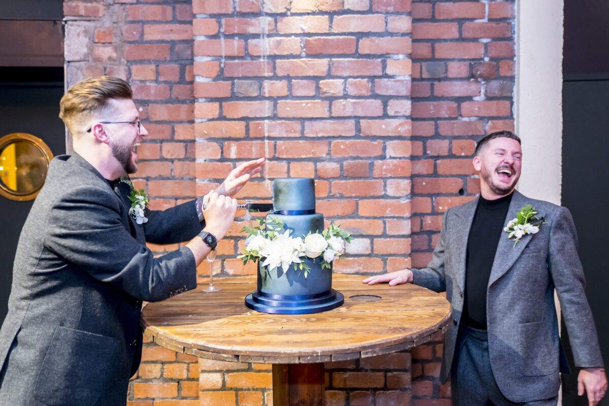 Two men laughing by wedding cake