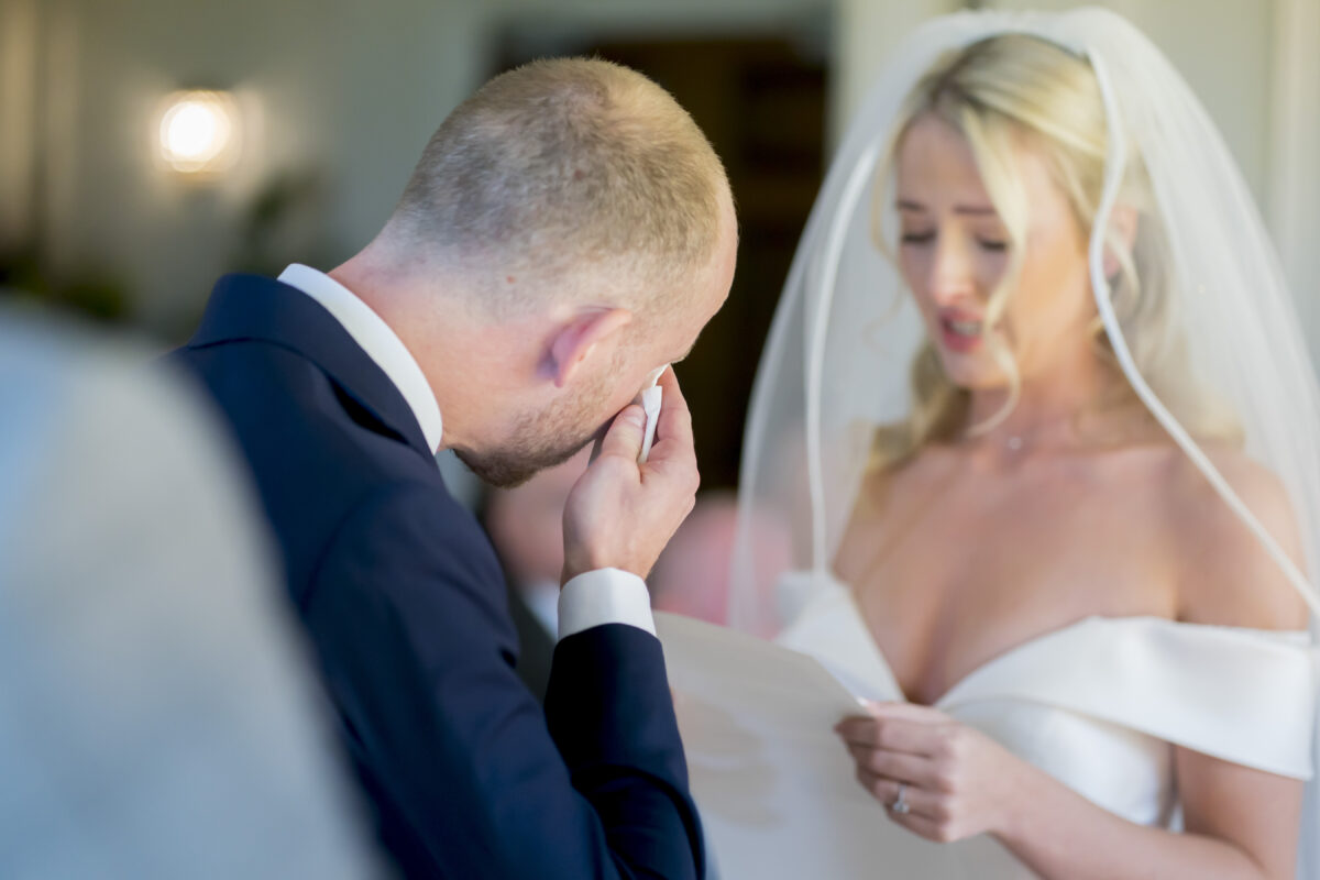 Bride reading vows, groom emotional at wedding.