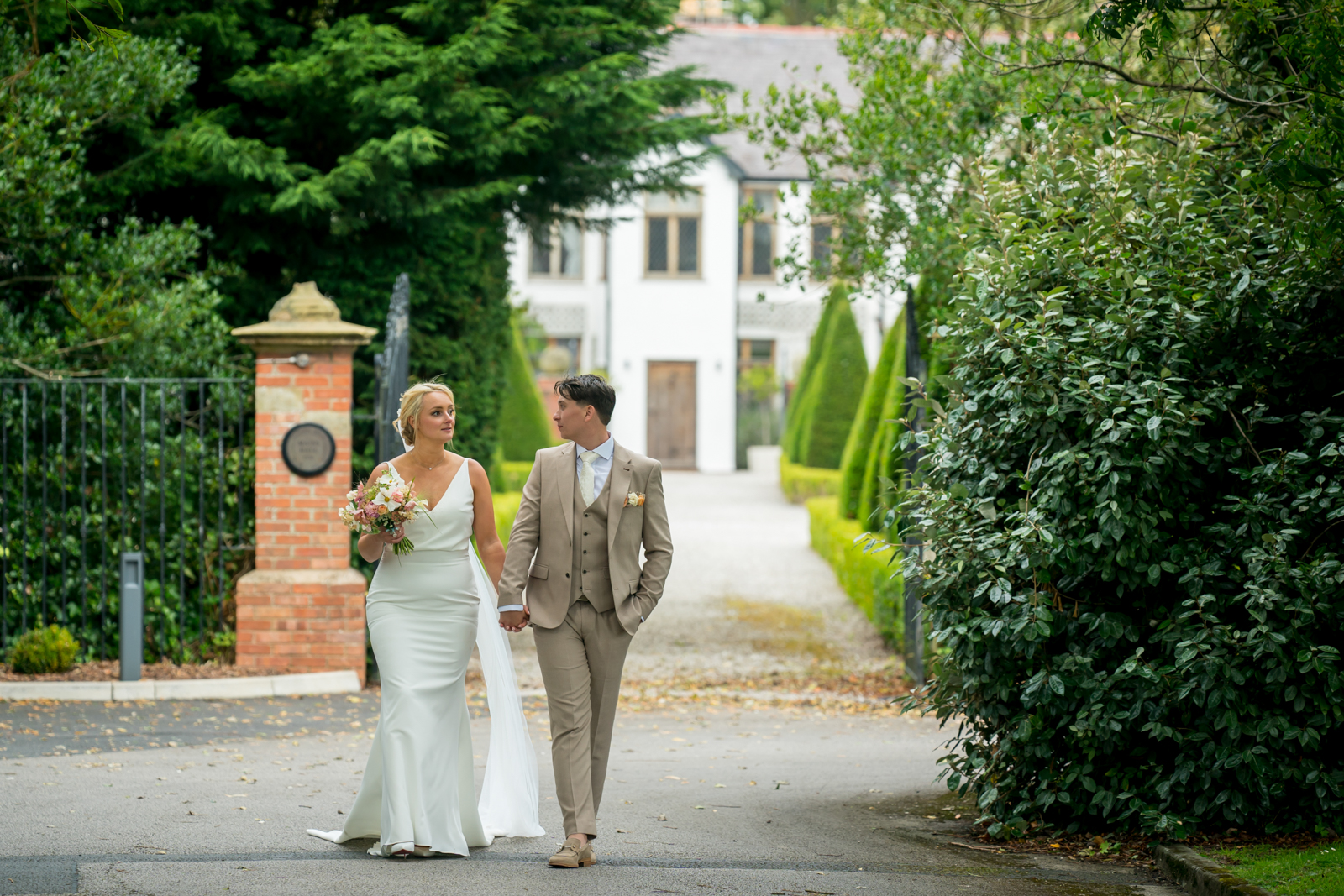 Bride and groom walking by elegant estate garden.