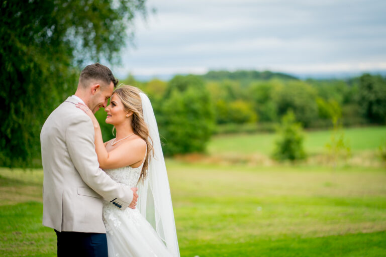 Bride and groom embracing outdoors in countryside wedding.