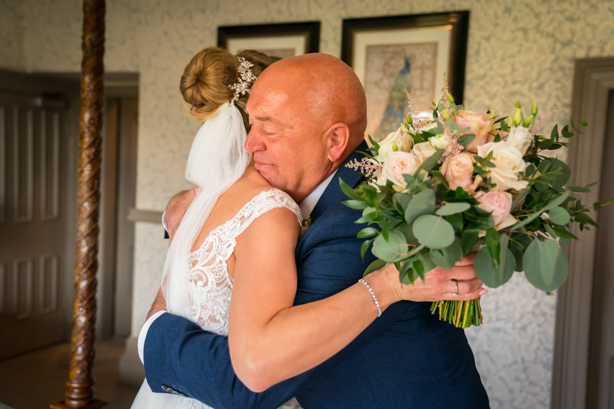Bride hugging man with bouquet indoors.