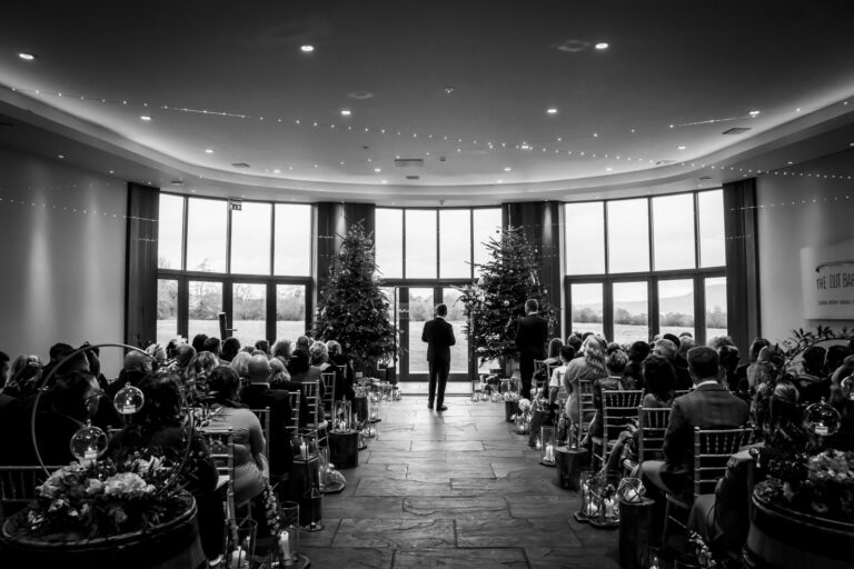 Indoor wedding ceremony with guests and trees.