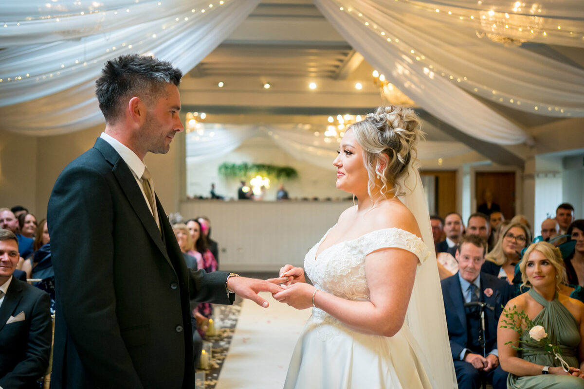 Bride places ring on groom during wedding ceremony.