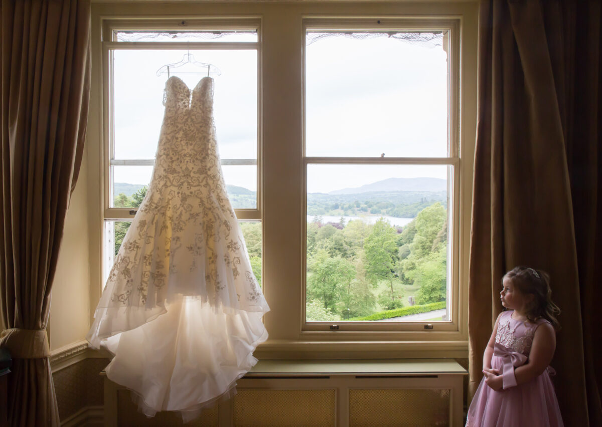 Wedding dress hanging, girl in pink dress watching.
