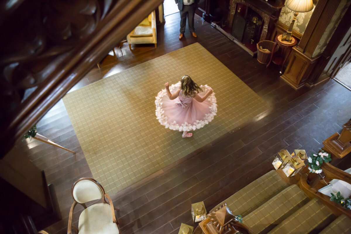 Girl in pink dress spinning in grand staircase hall.