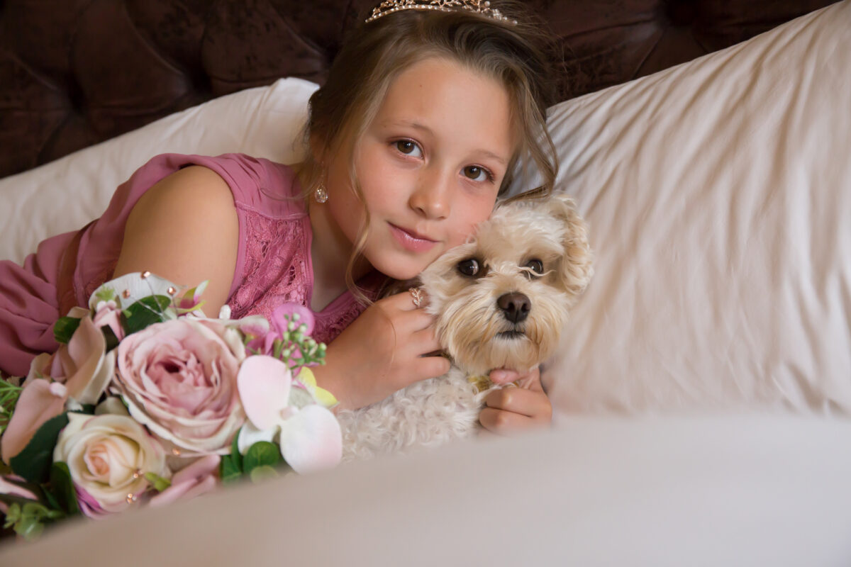 Girl hugging dog with flowers on bed