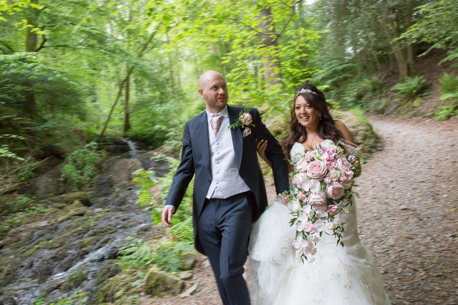 Bride and groom walking in lush green forest.