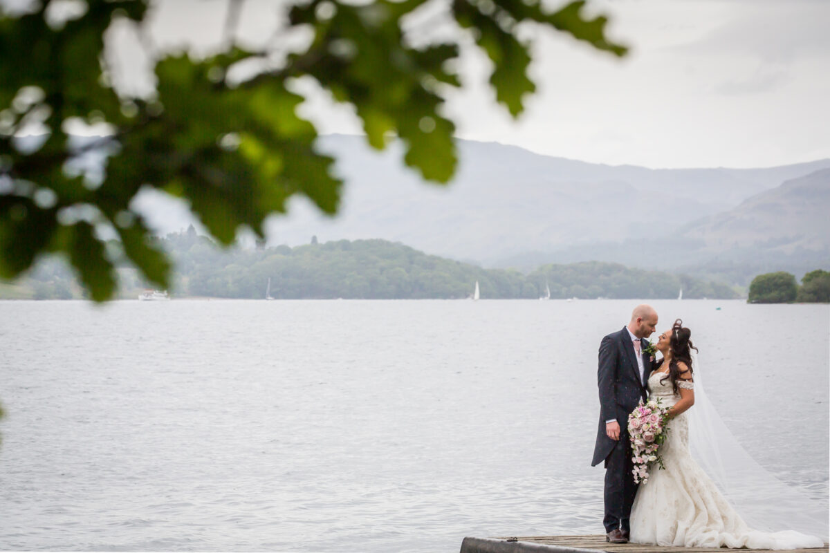 Wedding couple embraces by scenic lakeside.