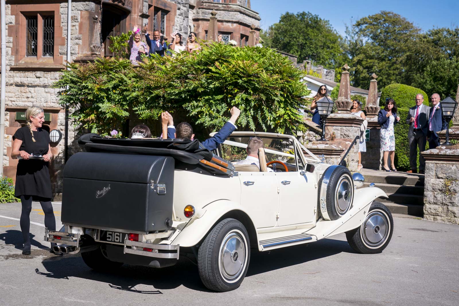 Vintage car leaving wedding reception at historic venue.