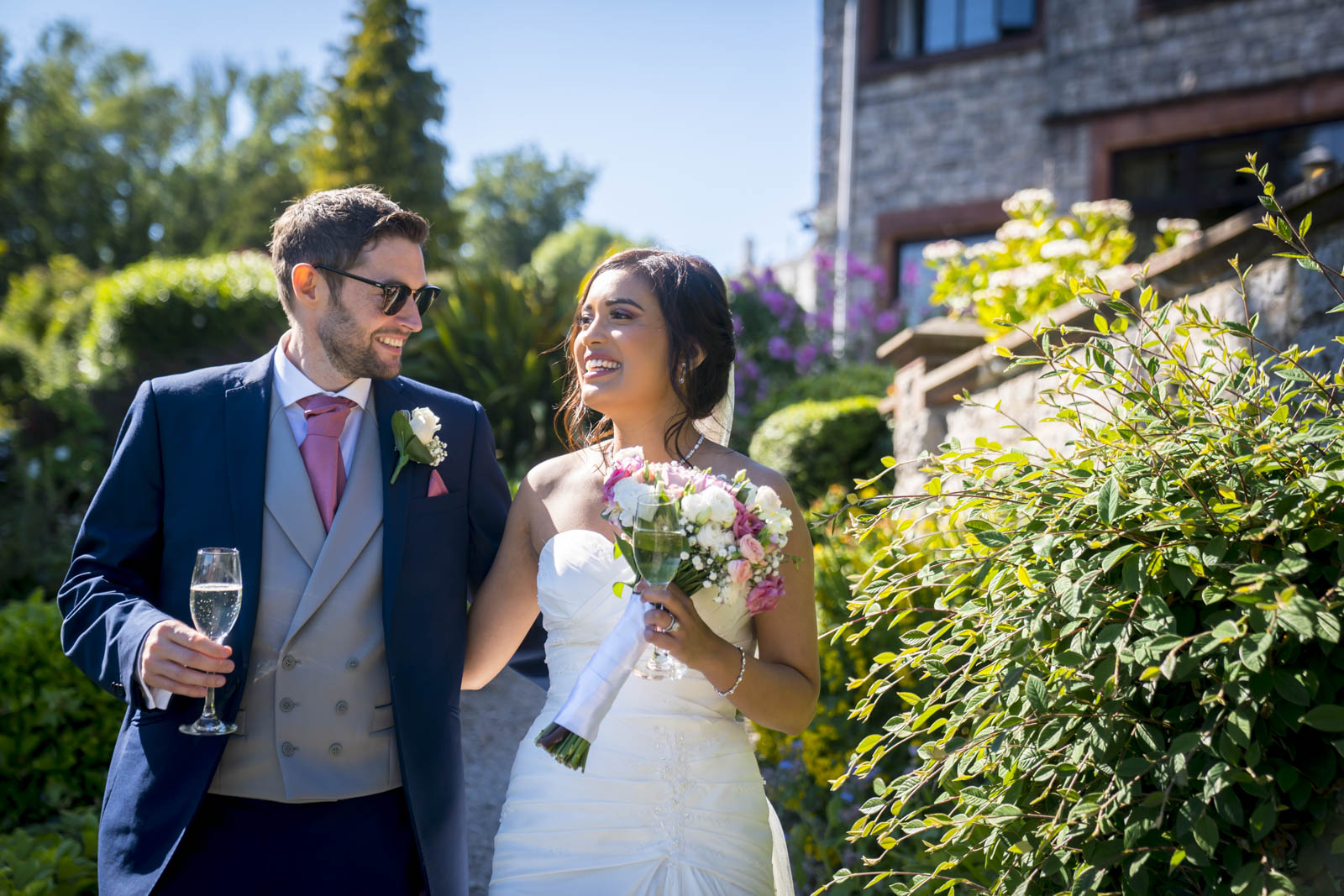 Bride and groom smiling outdoors, holding flowers.