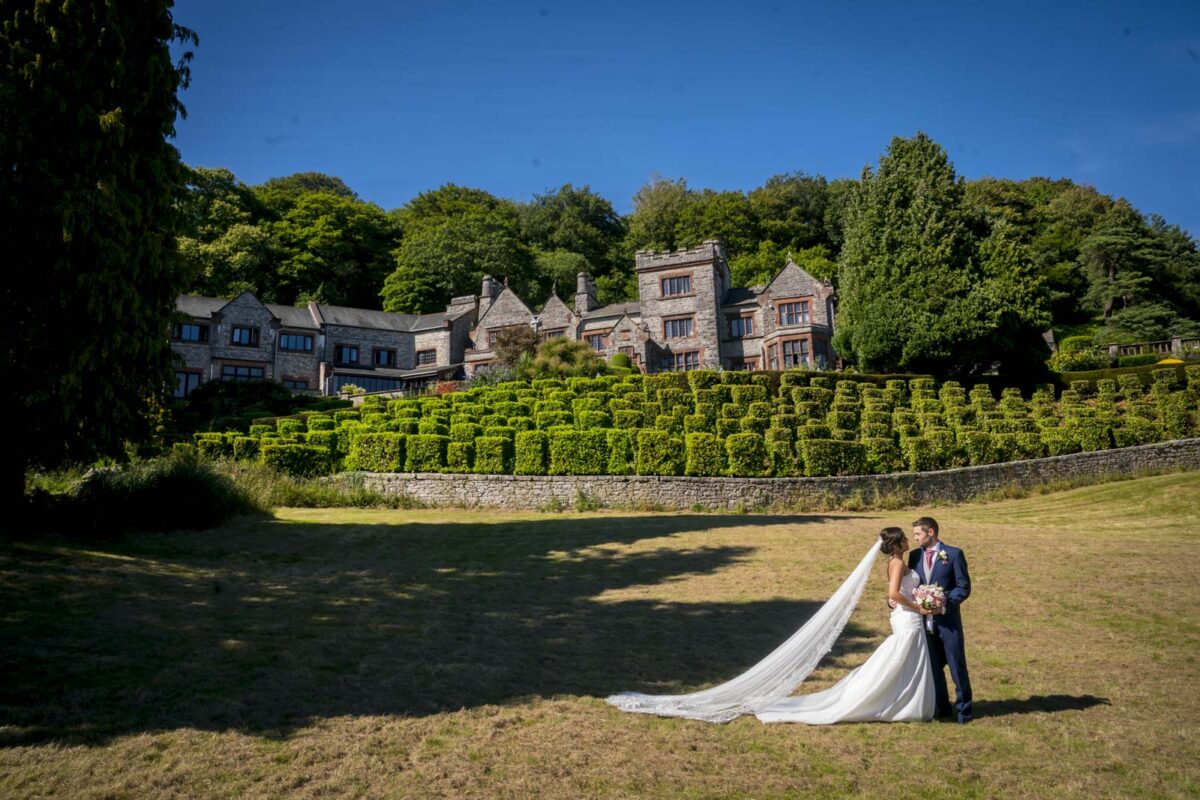 Wedding couple outside historic mansion, lush gardens surrounding.