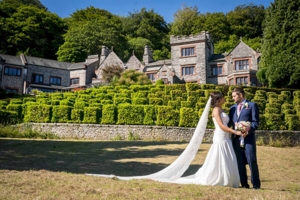 Bride and groom in lush garden before stone mansion.