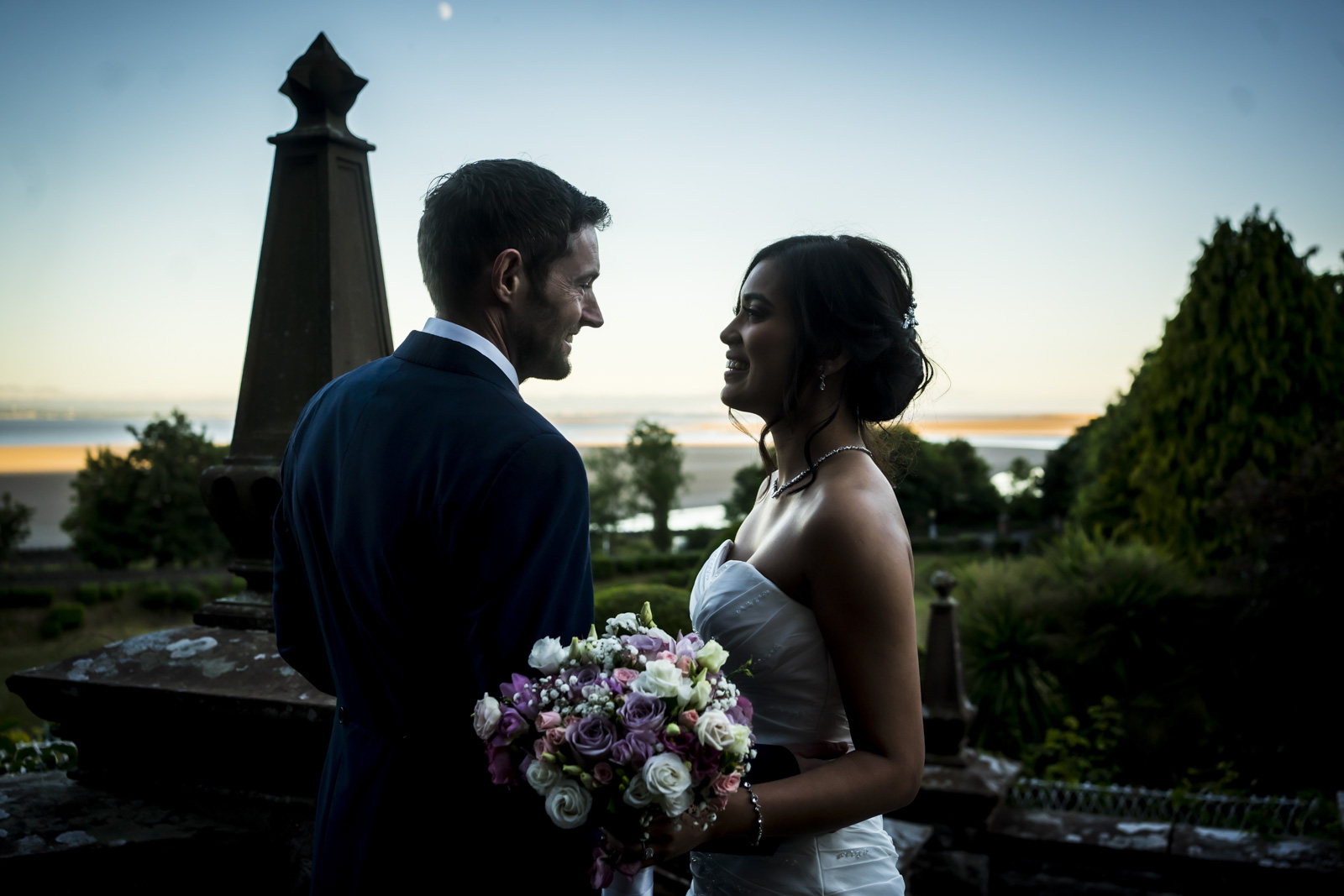 Wedding couple smiling at sunset with bouquet.
