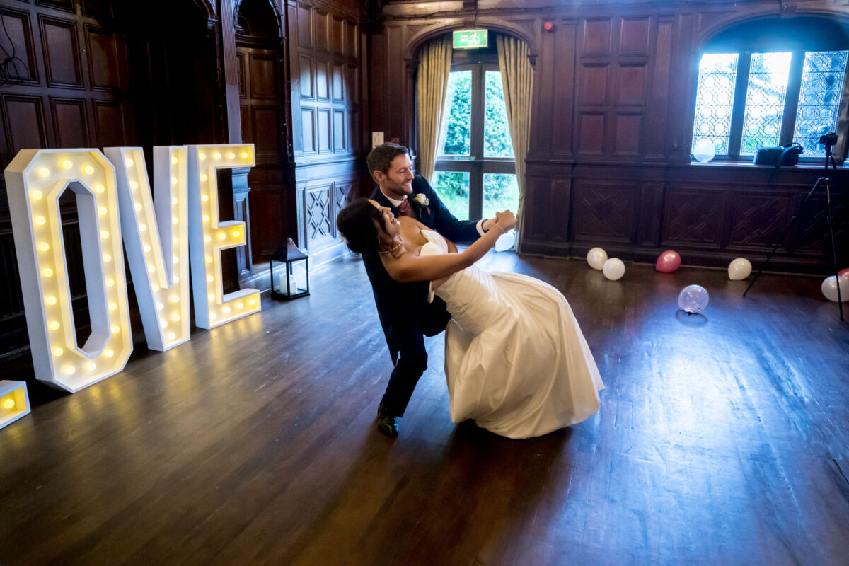 Couple dancing at wedding beside illuminated love sign.