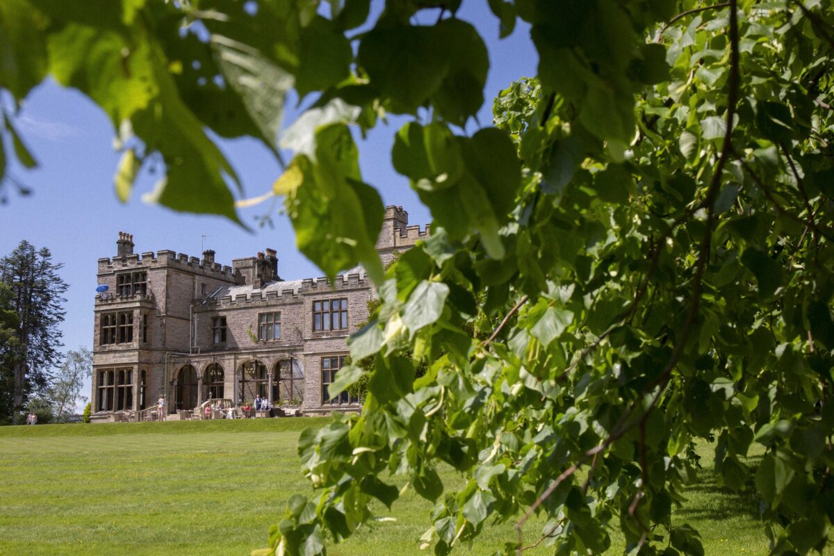 Historic stone mansion behind lush green trees.