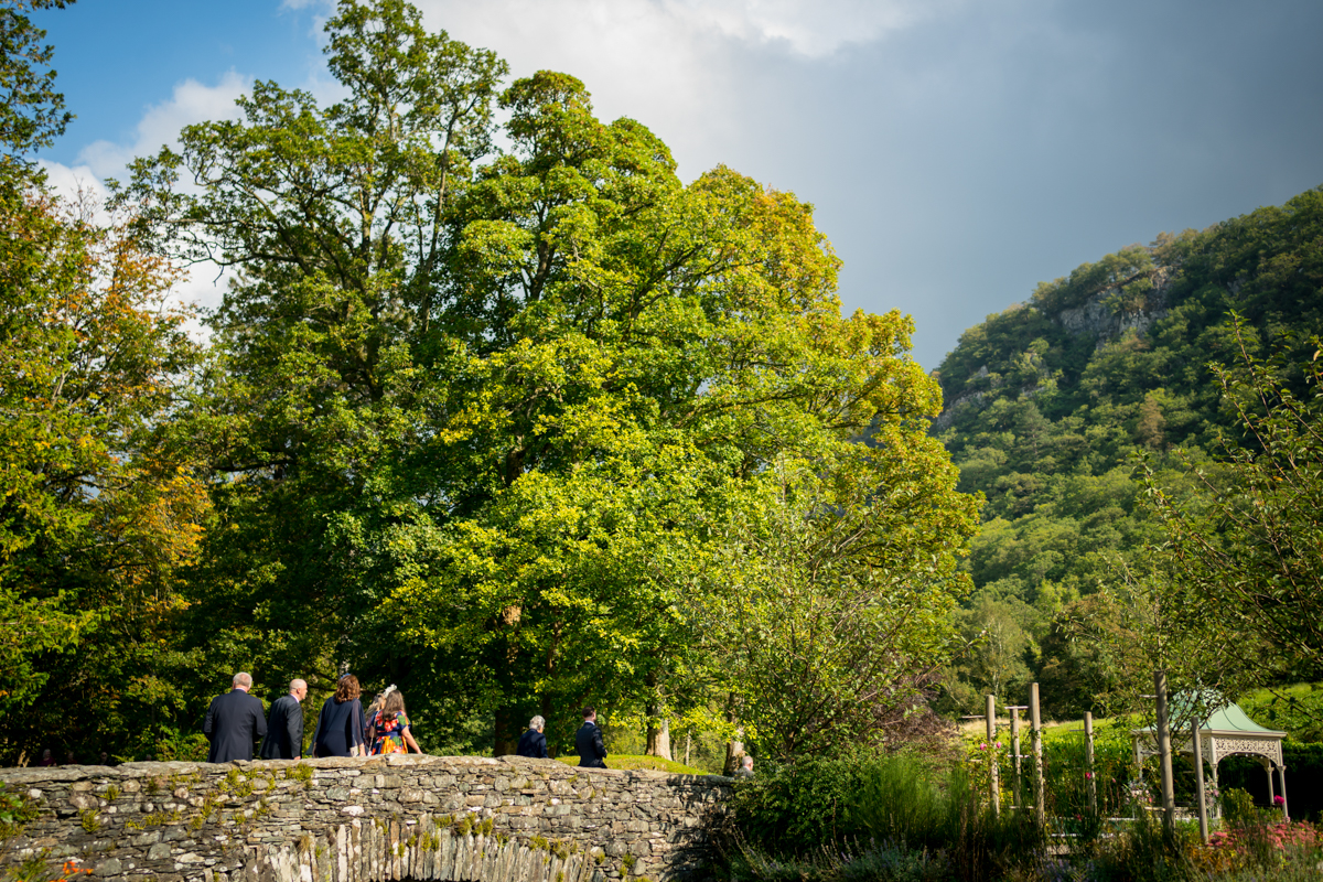 People walking on stone bridge in lush green landscape.