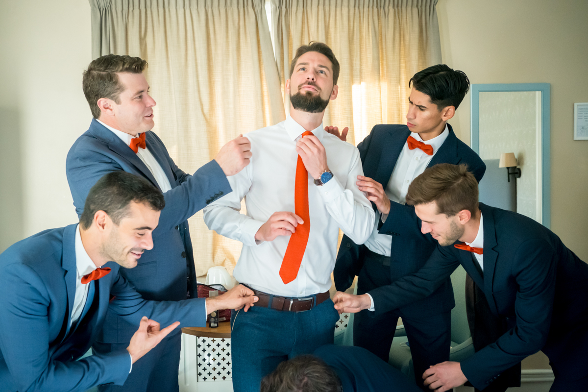 Groomsmen adjusting groom's tie before wedding ceremony.