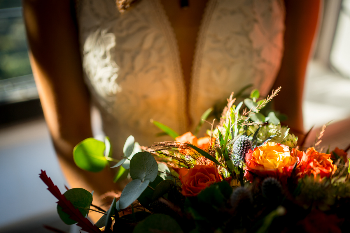 Bride in lace dress holding colourful bouquet.