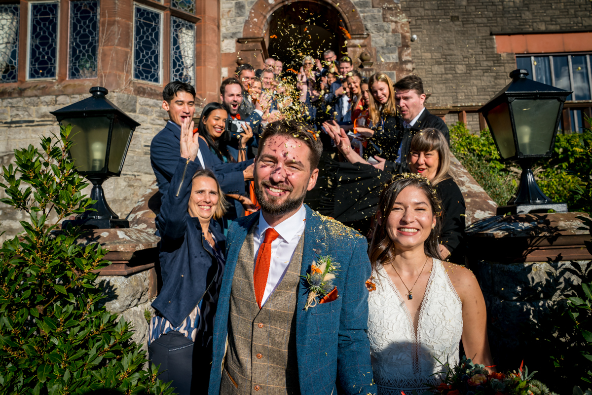 Smiling wedding couple with guests and confetti outside.