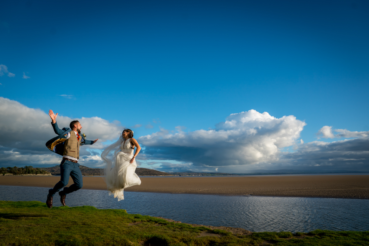Bride and groom joyfully jumping against blue sky