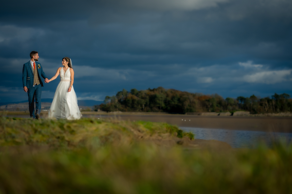 Bride and groom holding hands by the lake.