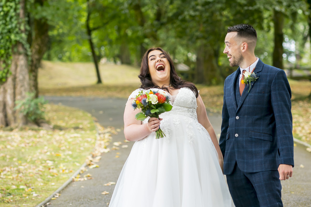 Bride and groom laughing in park