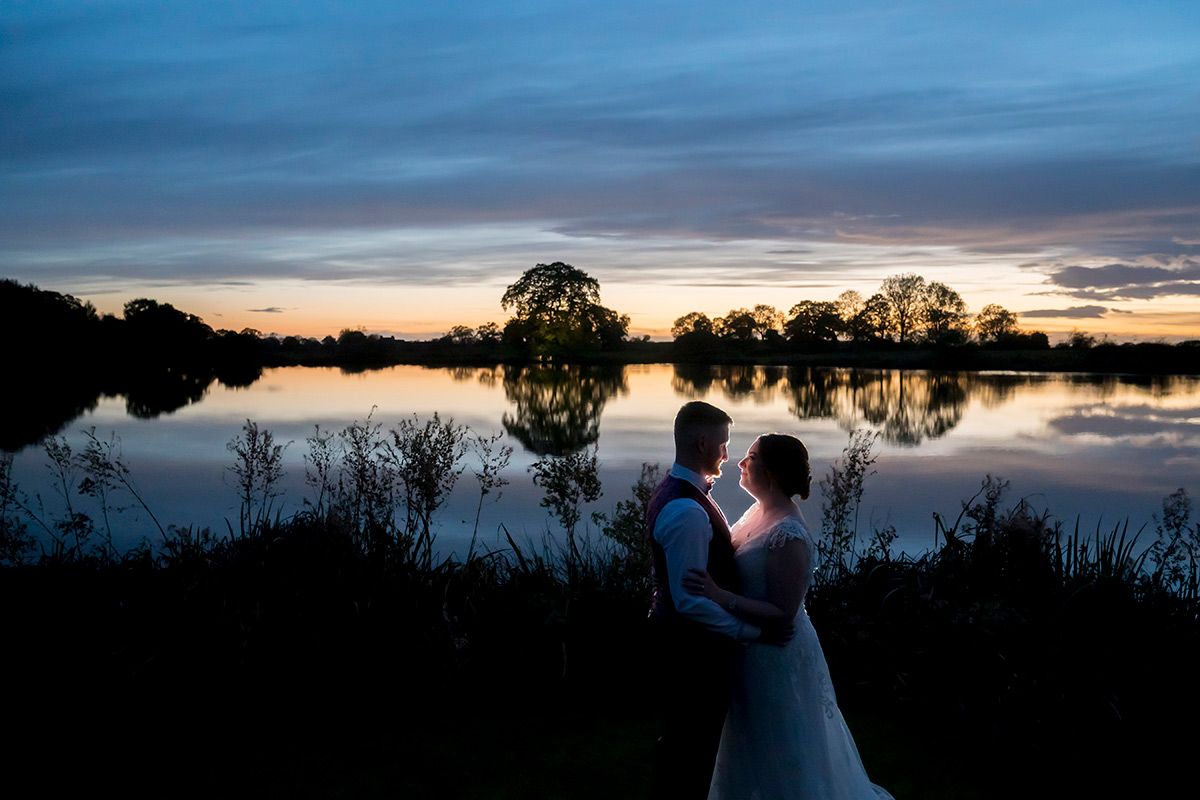Silhouetted couple embracing by lakeside at sunset