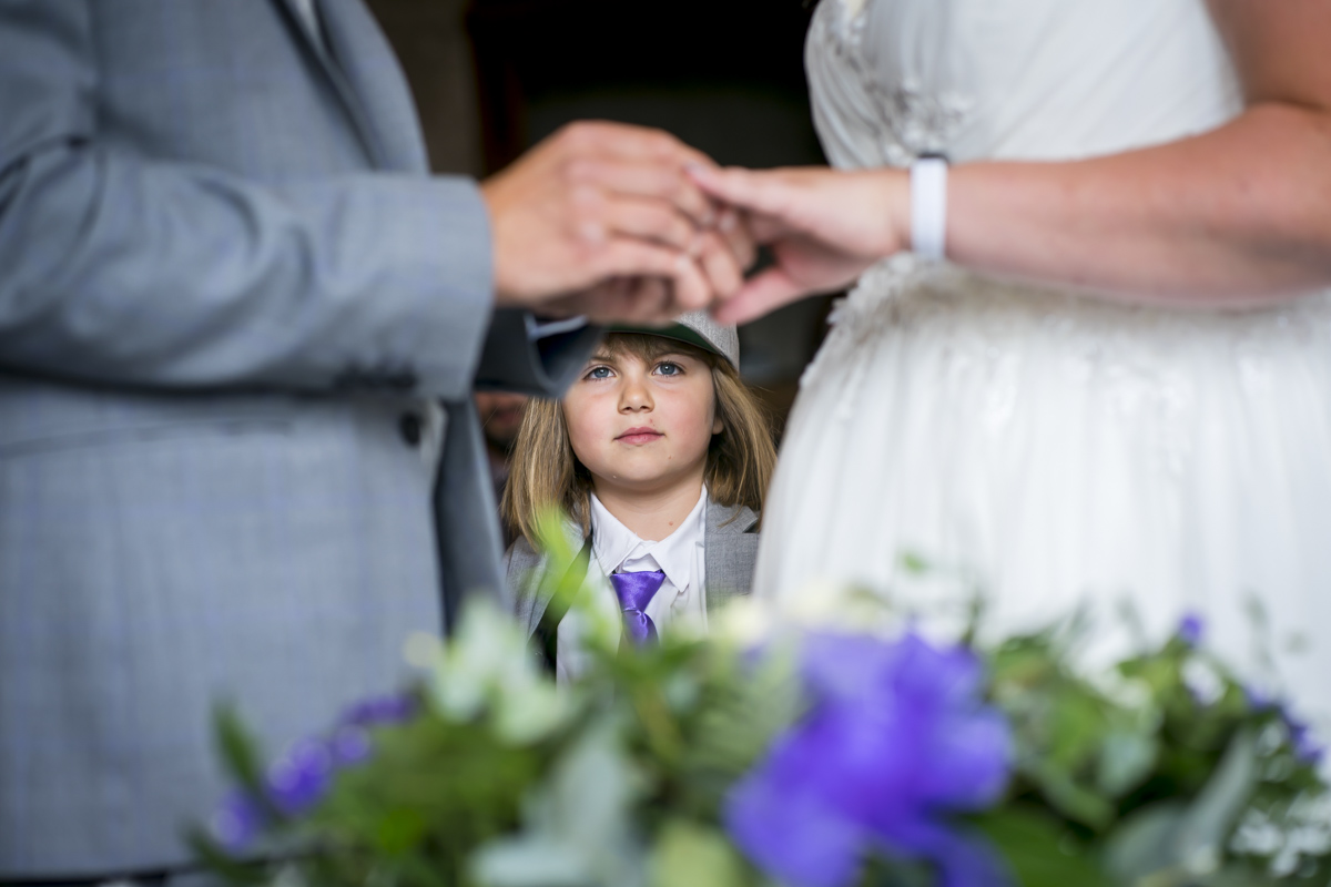 Child watching wedding ceremony with couple exchanging rings.