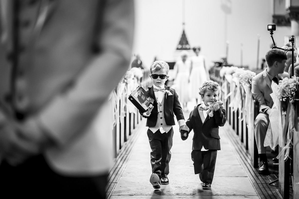 Children walking down wedding aisle in suits.