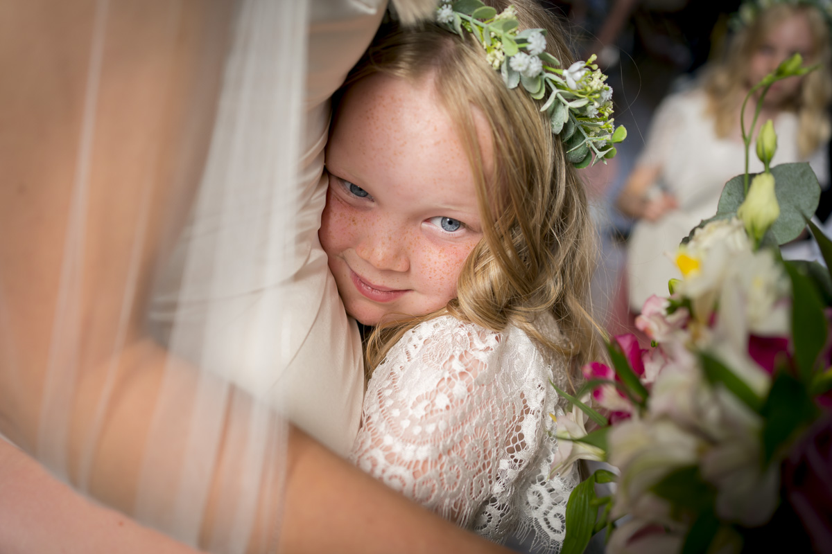 Young flower girl hugging bride at wedding.