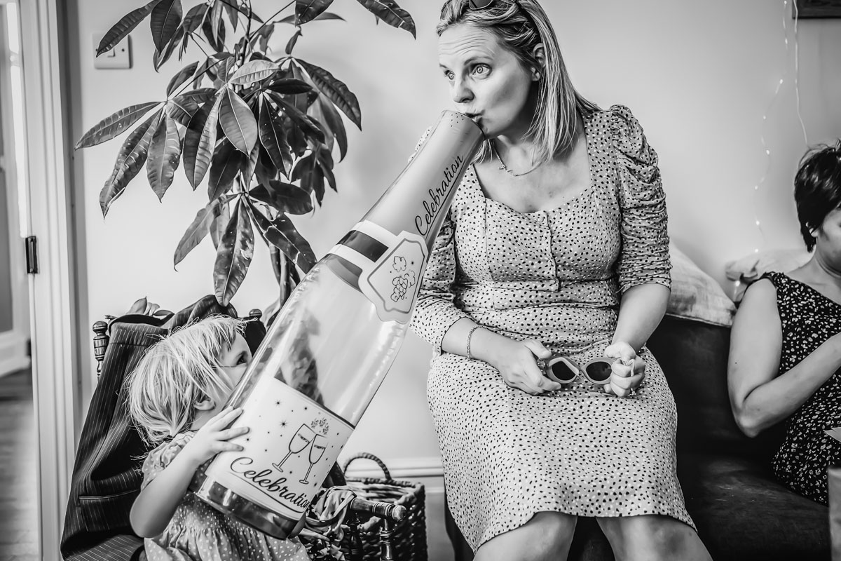 Woman with inflatable champagne bottle, child playing nearby.