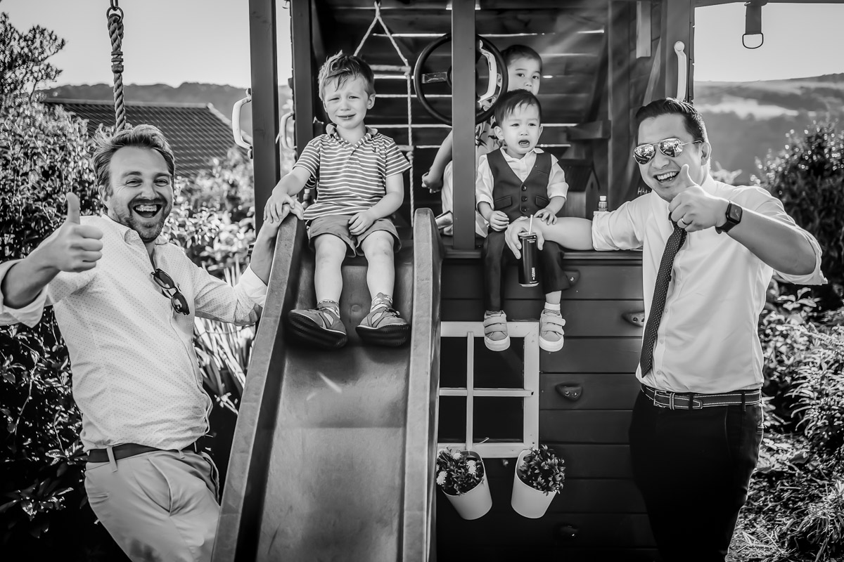 Adults and children smiling on playground slide, thumbs up.