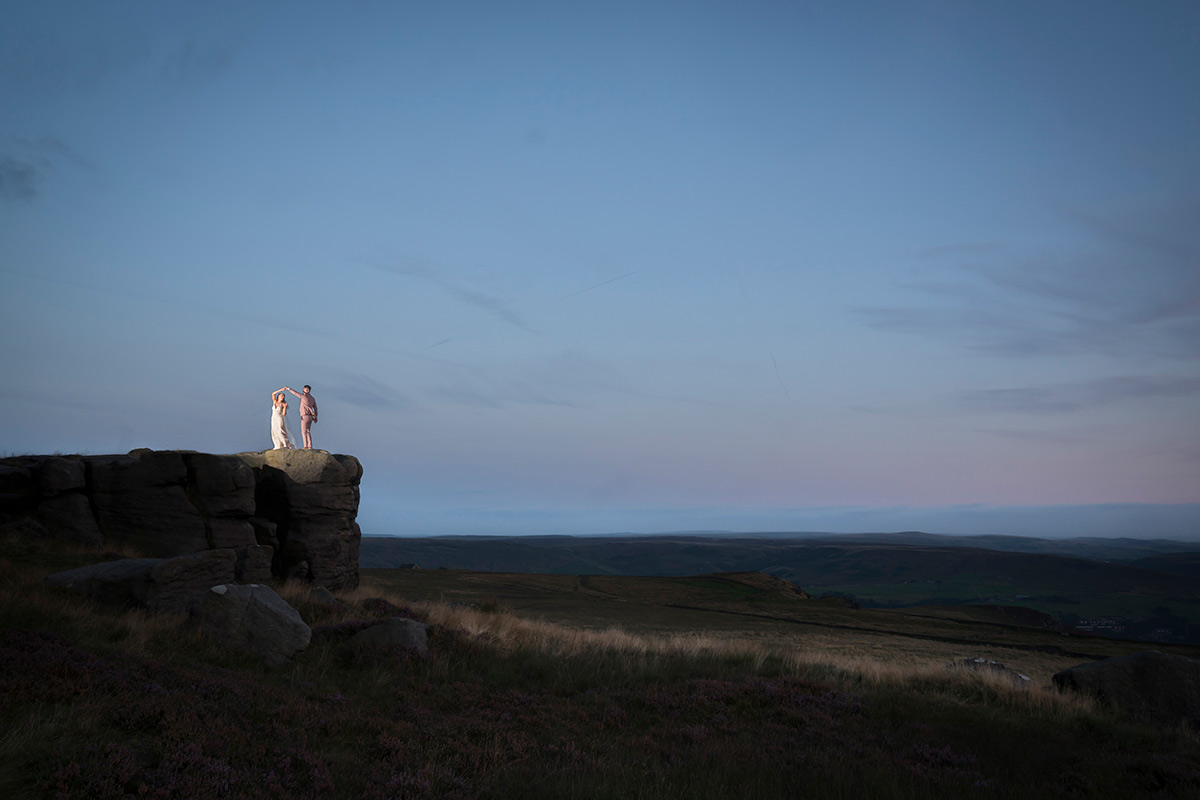 Couple on cliff at dusk in moorland landscape.