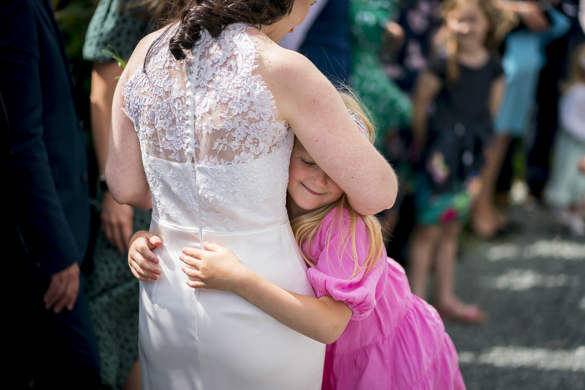 Child in pink hugs person in white dress.