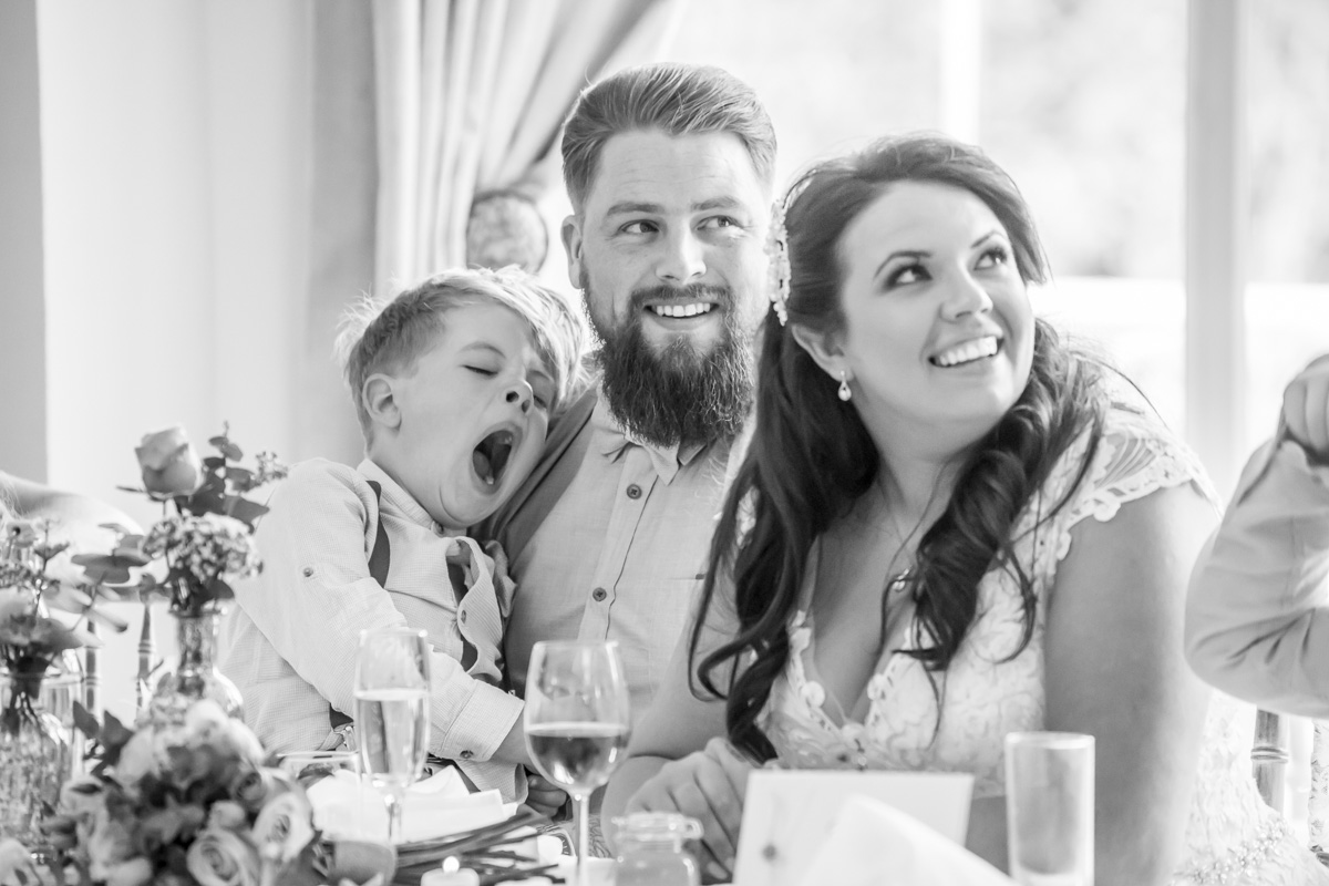 Family smiling at wedding table, child yawning.