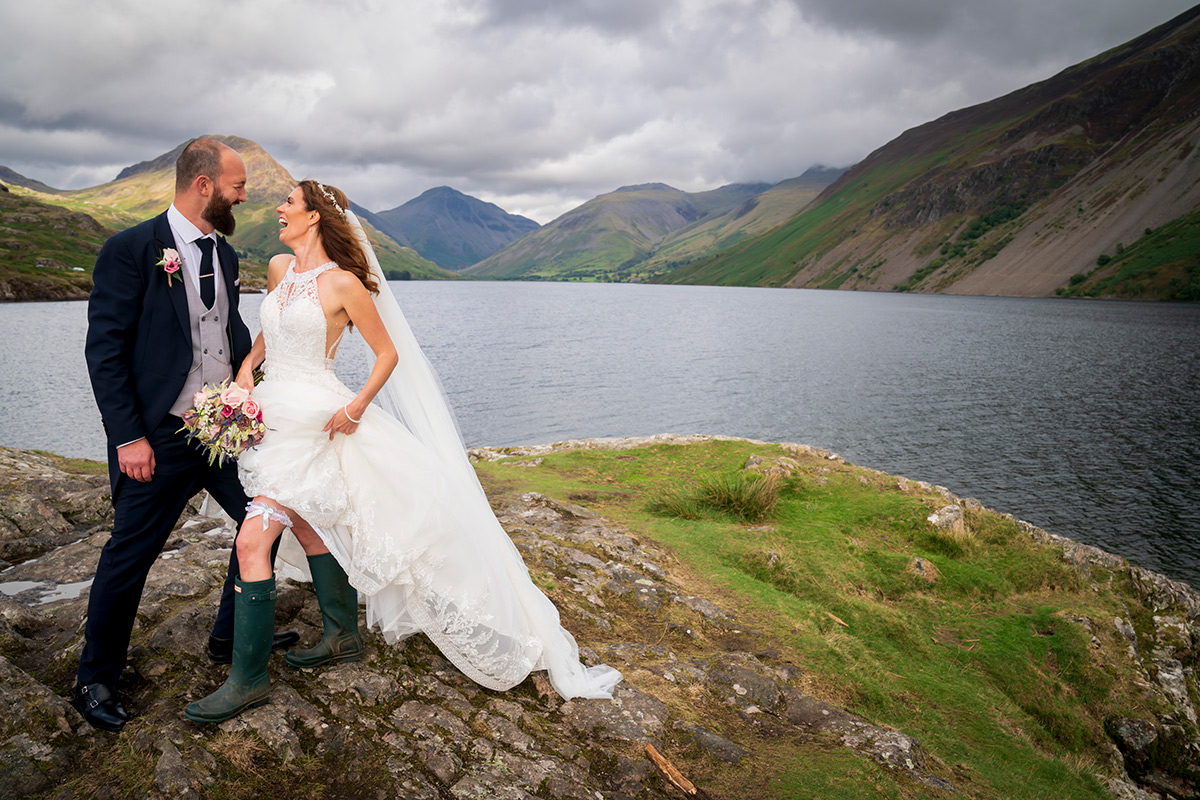 Wedding couple laughing by scenic lake and mountains.