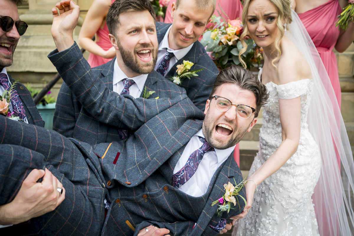 Groom party lifting groomsman, laughing at wedding celebration.