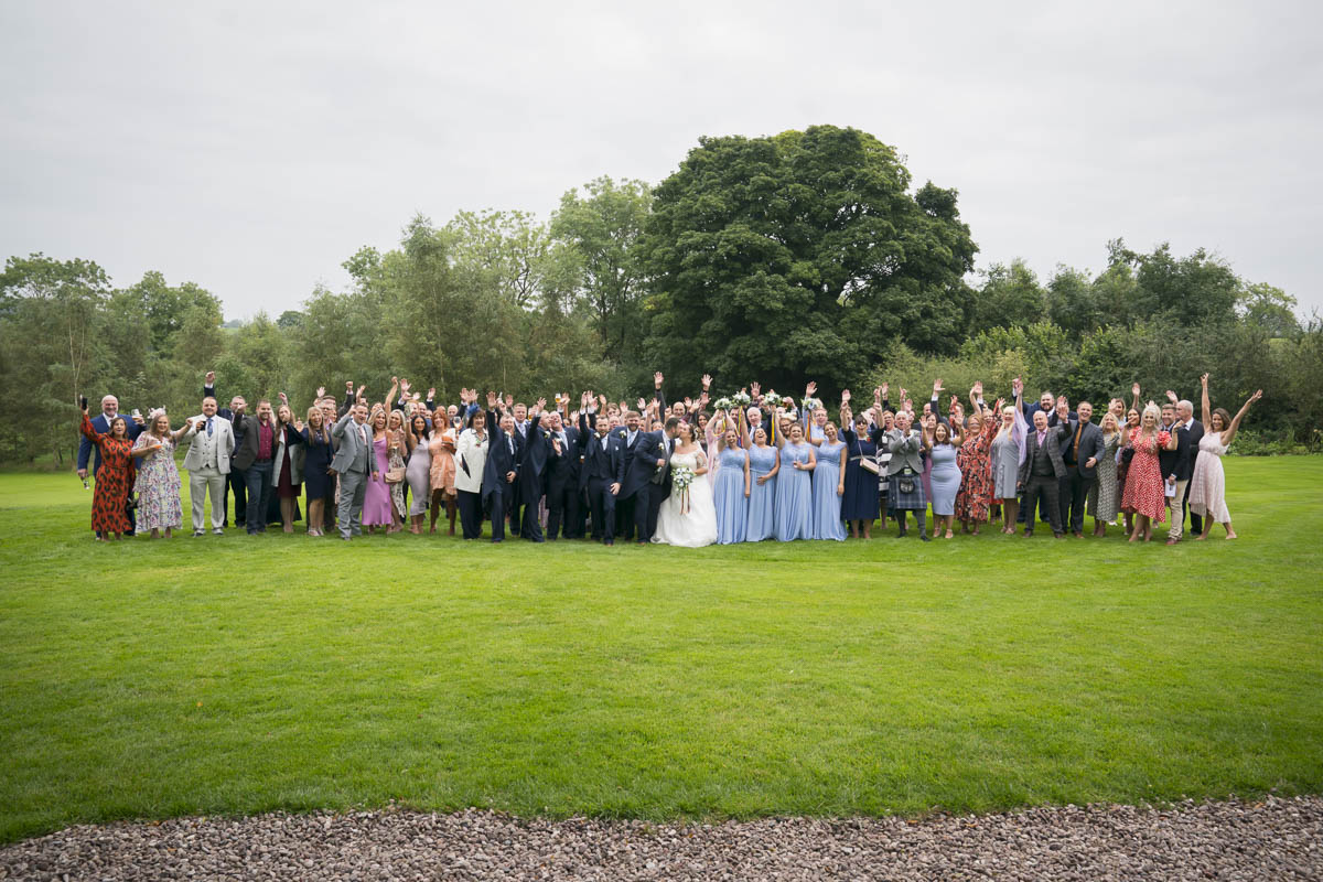 Large wedding party posing on green lawn.