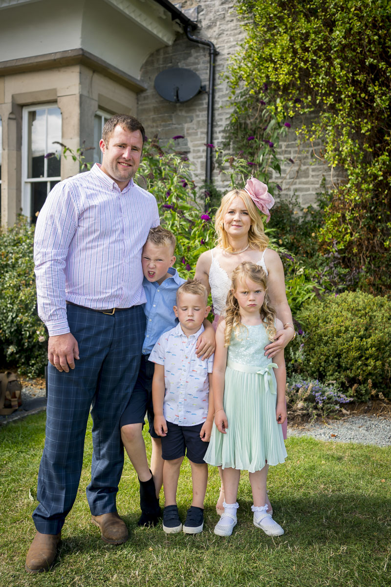 Family portrait outside house with garden backdrop.