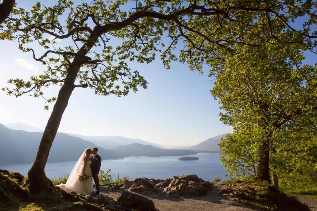Couple kissing by lake under tree, scenic view.