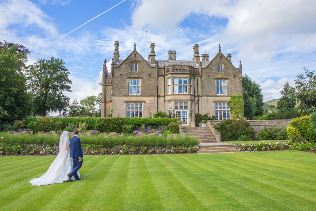 Wedding couple walking by grand estate, lush garden