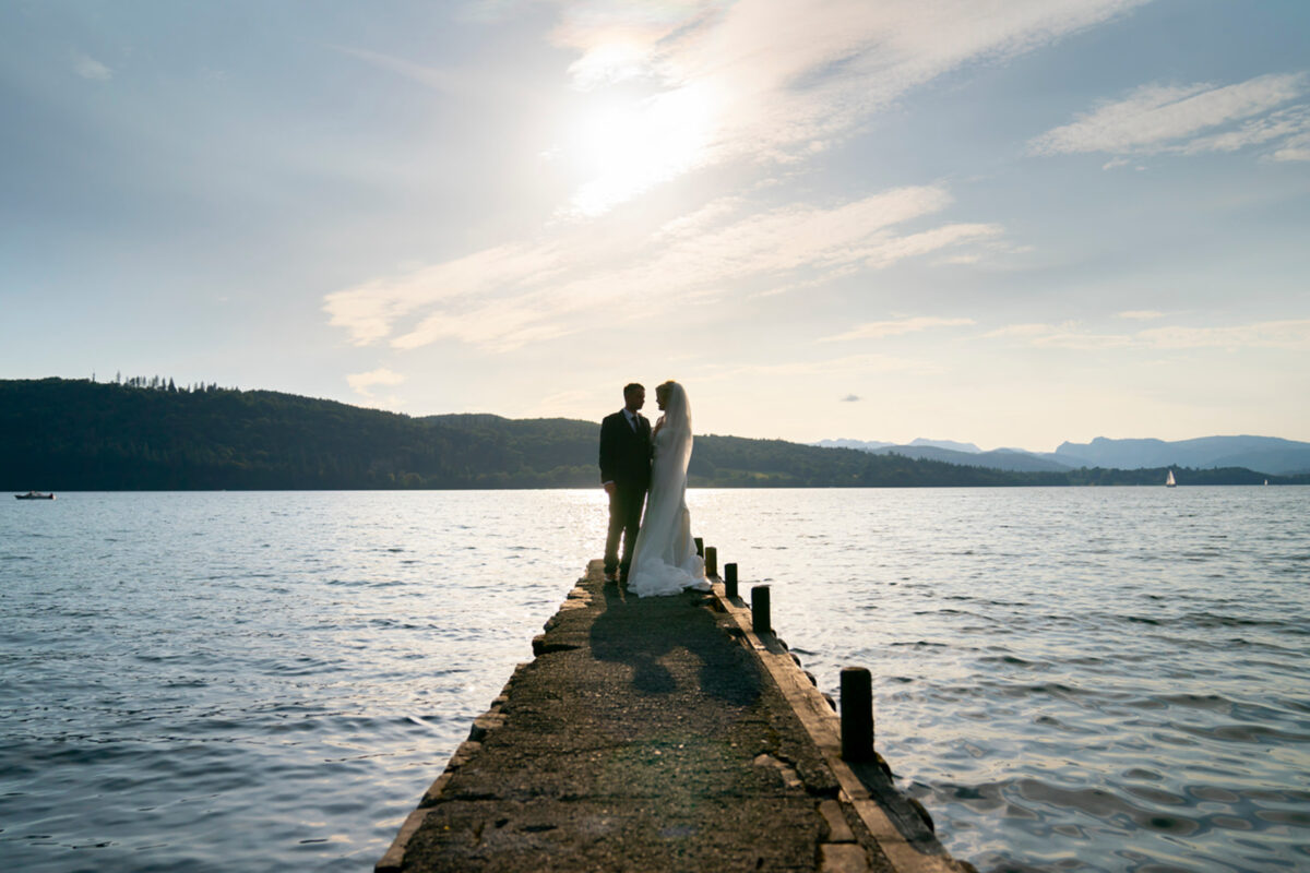 Wedding couple on pier by lake at sunset.