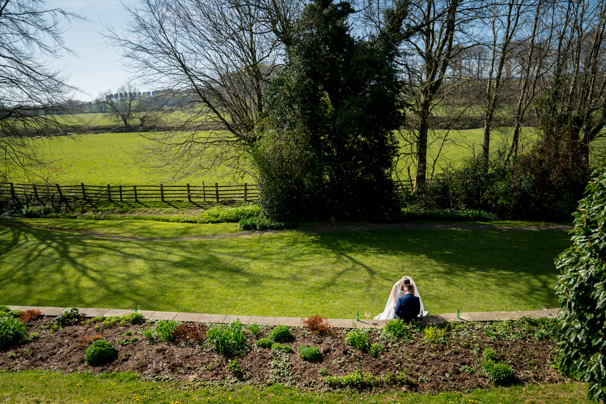 Bride and groom in garden, sunny countryside backdrop.