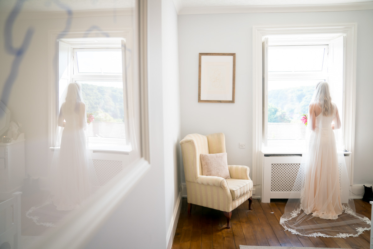 Bride in white dress looking out window