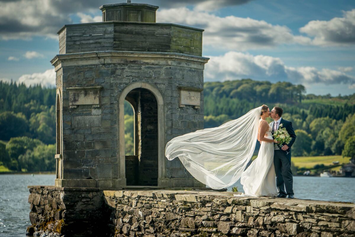 Bride and groom kissing by lake tower.