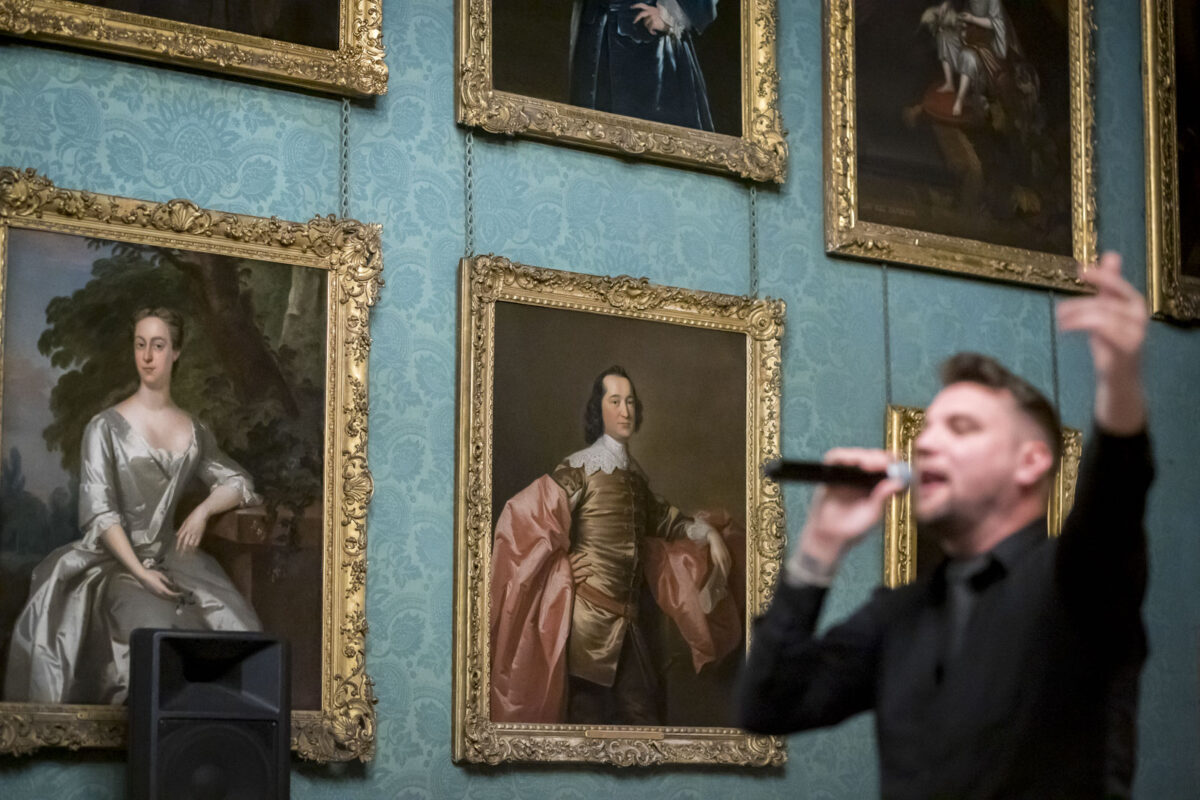 Singer performing in art gallery with portraits displayed.
