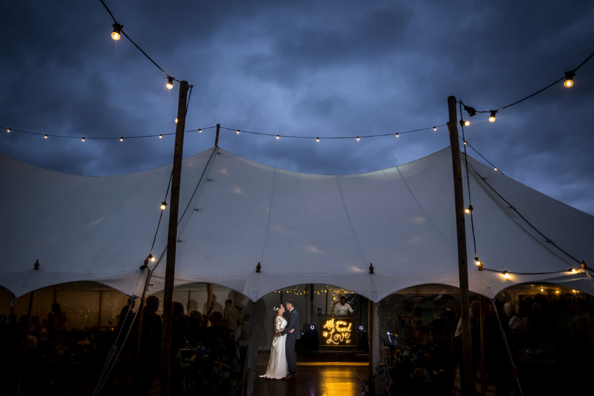 Wedding couple dancing under a lit tent canopy.